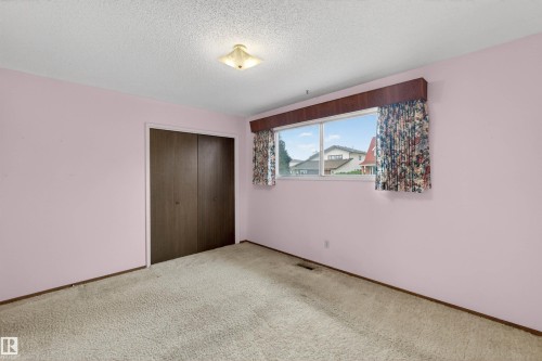 Carpeted room featuring a light fixture, a window with exterior visibility, and a built-in closet with bi-fold doors - 8407 150 Avenue, Edmonton, AB - Indoor Photo Showing Other Room