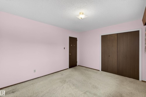 Carpeted room featuring a ceiling-mounted light fixture, a dark wood-finish door, and a two-panel dark wood-finish closet - 8407 150 Avenue, Edmonton, AB - Indoor Photo Showing Other Room