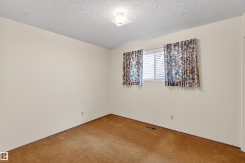Room featuring neutral painted walls, textured ceiling, a window with horizontal blinds, and a flush mount ceiling light fixture - 8407 150 Avenue, Edmonton, AB - Indoor Photo Showing Other Room