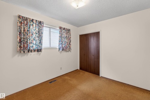 Room featuring a light-colored wall finish, textured ceiling, and a window with horizontal blinds - 8407 150 Avenue, Edmonton, AB - Indoor Photo Showing Other Room