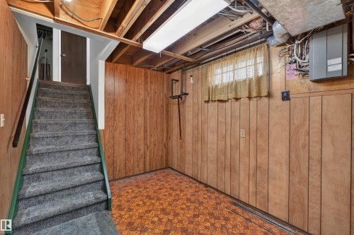 Lower level space featuring wood-look paneling, exposed ceiling joists, and patterned flooring - 8407 150 Avenue, Edmonton, AB - Indoor Photo Showing Basement