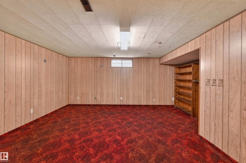 Spacious room with wood-panel walls, patterned red carpeting, and a drop ceiling - 8407 150 Avenue, Edmonton, AB - Indoor