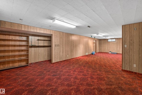 Spacious lower-level room featuring wood-panel walls and a patterned red carpet - 8407 150 Avenue, Edmonton, AB - Indoor