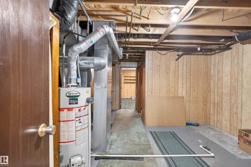 Utility space featuring a water heater, exposed ductwork, wood-paneled walls, and visible ceiling joists - 8407 150 Avenue, Edmonton, AB - Indoor Photo Showing Basement