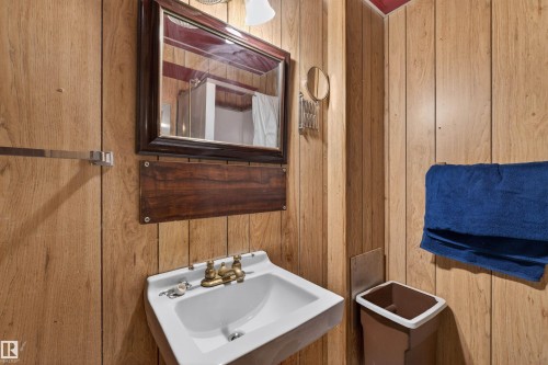Bathroom featuring wood-paneled walls, a wall-mounted white sink with brass-toned fixtures, and a framed mirror - 8407 150 Avenue, Edmonton, AB - Indoor Photo Showing Bathroom