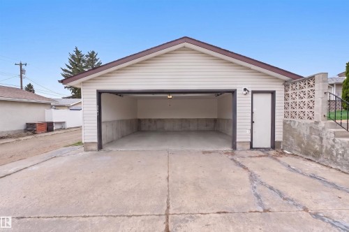 Detached garage featuring light-colored siding, a brown trimmed gable roof, and a pedestrian access door - 8407 150 Avenue, Edmonton, AB - Outdoor