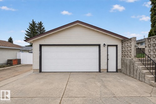 Detached garage featuring light-colored siding, a white overhead door, and a brown trimmed roofline - 8407 150 Avenue, Edmonton, AB - Outdoor With Exterior