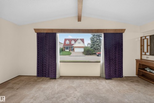 Spacious interior featuring a large picture window, vaulted ceiling with exposed beam, and plush carpeting - 8407 150 Avenue, Edmonton, AB - Indoor