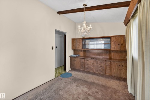 Room featuring a crystal chandelier, wood-finish ceiling beams, and a built-in wood-finish cabinet with glass-front uppers and lower storage - 8407 150 Avenue, Edmonton, AB - Indoor Photo Showing Other Room
