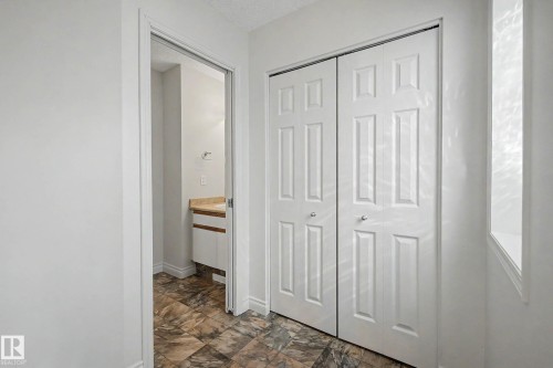 Hallway featuring two-panel bifold closet doors, patterned floor tiling, and a partial view into a bathroom with a vanity and wood-finish countertop - 16211 55A Street, Edmonton, AB - Indoor Photo Showing Other Room