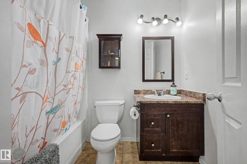 Full bathroom featuring a white bathtub with shower, a toilet, and a dark wood-finish vanity with a single basin sink and a patterned countertop - 16211 55A Street, Edmonton, AB - Indoor Photo Showing Bathroom