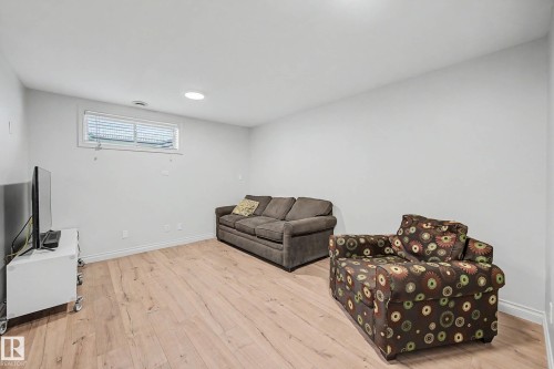 Expansive room featuring wood-finish flooring, light-colored walls, a single window with blinds, baseboard trim, and a ceiling light fixture - 16211 55A Street, Edmonton, AB - Indoor Photo Showing Basement