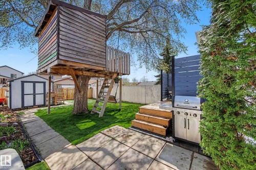 Expansive backyard featuring a mature tree with a built-in treehouse, a manicured lawn, a large storage shed, and a privacy fence - 16211 55A Street, Edmonton, AB - Outdoor