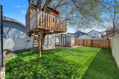 Expansive backyard featuring a treehouse structure, artificial turf, wood picket fencing, and a storage shed - 16211 55A Street, Edmonton, AB - Outdoor