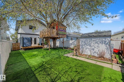 Spacious backyard featuring artificial turf, a mature shade tree, and a built-in treehouse structure - 16211 55A Street, Edmonton, AB - Outdoor