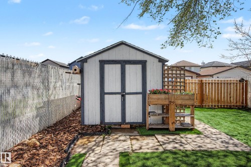 Backyard featuring a white storage shed with dark trim, a wooden raised garden bed, and a manicured lawn - 16211 55A Street, Edmonton, AB - Outdoor