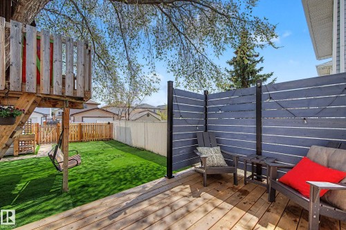 Expansive backyard featuring a wood deck, artificial turf, a privacy fence with string lighting, and a multi-level wooden play structure - 16211 55A Street, Edmonton, AB - Outdoor With Deck Patio Veranda