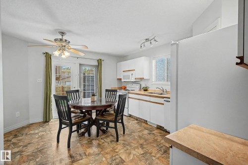 Kitchen and dining area featuring white cabinetry, light wood-finish countertops, stainless steel sink, and white appliances - 16211 55A Street, Edmonton, AB - Indoor