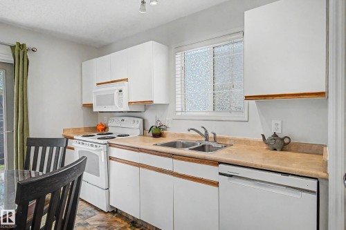 Kitchen featuring white cabinetry, light countertops, and coordinating white appliances - 16211 55A Street, Edmonton, AB - Indoor Photo Showing Kitchen With Double Sink