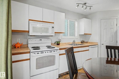 Kitchen featuring white cabinetry with wood trim, a white oven, and a white over-the-range microwave - 16211 55A Street, Edmonton, AB - Indoor Photo Showing Kitchen With Double Sink
