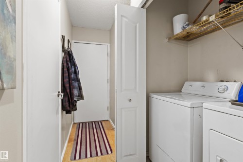 Dedicated laundry area featuring a white washing machine and dryer, overhead wire shelving, and wood-finish flooring - 6 3803 76 Street, Edmonton, AB - Indoor Photo Showing Laundry Room