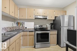 Kitchen featuring light-toned cabinetry, a stainless steel range, a stainless steel refrigerator, dark countertops, and a mosaic tile backsplash - 