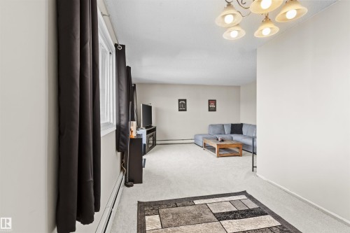 Carpeted living area featuring a large window, warm neutral wall tones, and a multi-light ceiling fixture - 6 3803 76 Street, Edmonton, AB - Indoor Photo Showing Other Room