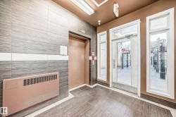 Building entrance featuring a light brown elevator door, wood-finish flooring, and grey tiled walls with a white accent band - 