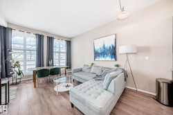Spacious living area featuring wood-finish flooring, high ceilings, and expansive windows with dark drapery - 