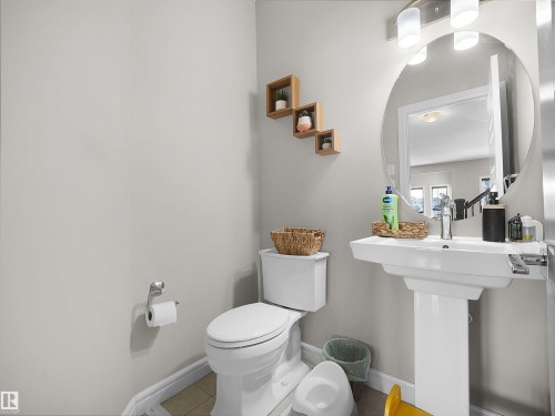Pedestal sink with single-handle faucet, circular mirror, and modern vanity lighting - 3247 15 Avenue Nw, Edmonton, AB 