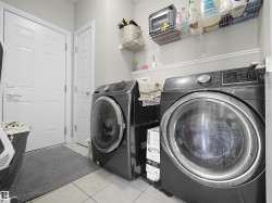 Dedicated laundry area featuring a front-loading washer and dryer set, white paneled doors, wall-mounted wire shelving, and neutral floor tile - 