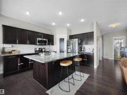Kitchen featuring dark wood cabinetry, stainless steel appliances, a white tile backsplash, and a large central island with a granite countertop and sink - 