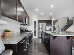 Kitchen featuring dark wood cabinetry, light granite countertops, stainless steel appliances, and recessed lighting - 