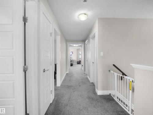 Carpeted hallway with light gray walls, white trim, and paneled doors featuring silver-tone hardware - 3247 15 Avenue Nw, Edmonton, AB 
