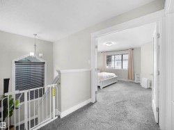 Carpeted hallway with white baseboards and trim, featuring a contemporary chandelier and an architectural window with blinds - 