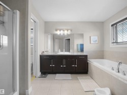 Spacious bathroom featuring a dual vanity with a granite-style countertop, a built-in bathtub, a separate shower enclosure, and tiled flooring - 