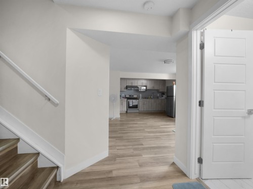 Open concept living space featuring a modern kitchen with grey cabinetry, stainless steel appliances, and a wood-finish flooring throughout - 3247 15 Avenue Nw, Edmonton, AB 