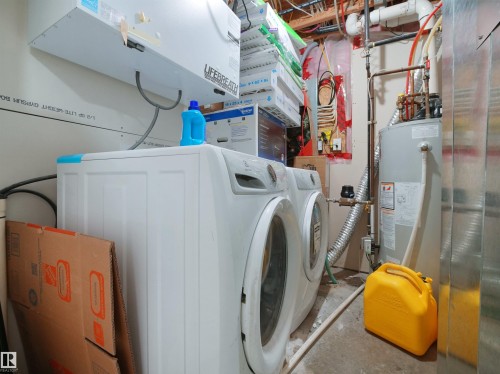Laundry area featuring a side-by-side washer and dryer, a water heater, and exposed utility lines - 3247 15 Avenue Nw, Edmonton, AB 
