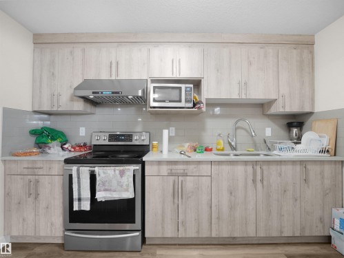 Kitchen featuring wood-finish cabinetry, stainless steel range with overhead ventilation, undermount sink, and a microwave built into upper cabinetry - 3247 15 Avenue Nw, Edmonton, AB 