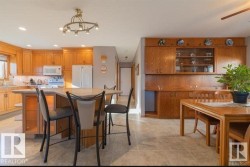 Open-concept kitchen and dining area featuring warm-toned cabinetry, a spacious kitchen island with seating, recessed lighting, and tile flooring - 