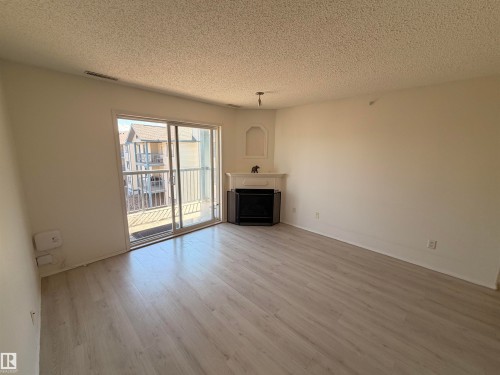 Living area featuring light wood-finish flooring, white walls, and a corner fireplace with a decorative mantel and niche - 424 16303 95 Street, Edmonton, AB - Indoor Photo Showing Living Room With Fireplace