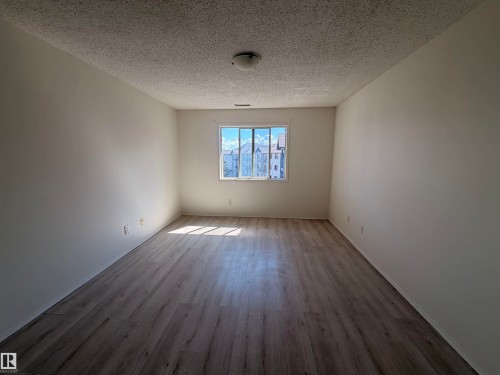 Bright interior space featuring a window with exterior residential structures visible, wood-finish flooring, white walls, and a textured ceiling with a flush-mount light fixture - 424 16303 95 Street, Edmonton, AB - Indoor Photo Showing Other Room