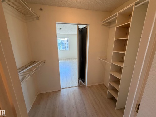 Walk-in closet featuring light wood-finish flooring, built-in shelving, hanging rods, and wire shelving units - 424 16303 95 Street, Edmonton, AB - Indoor With Storage
