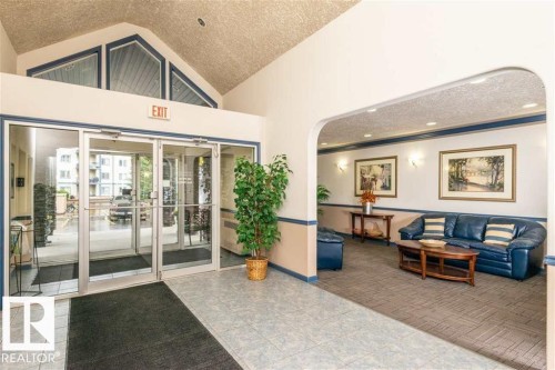 Lobby featuring a double glass entry door, vaulted ceiling with transom windows, recessed lighting, and a separate seating area with wall sconces - 424 16303 95 Street, Edmonton, AB -  With Exterior