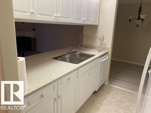 Kitchen featuring white cabinetry, dual basin stainless steel sink, integrated dishwasher, and a light-toned countertop - 424 16303 95 Street, Edmonton, AB - Indoor Photo Showing Kitchen With Double Sink