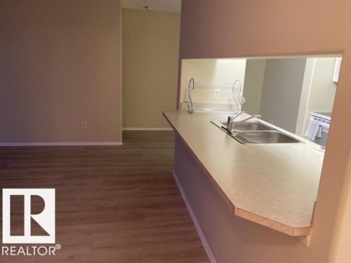 Kitchen pass-through featuring a double basin stainless steel sink and a light-toned countertop - 424 16303 95 Street, Edmonton, AB - Indoor Photo Showing Other Room