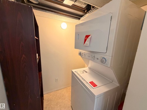 Laundry area featuring a white stacked washer and dryer unit, neutral wall paint, and light-toned floor tiles - 424 16303 95 Street, Edmonton, AB - Indoor Photo Showing Laundry Room