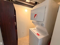 Laundry area featuring a white stacked washer and dryer unit, neutral wall paint, and light-toned floor tiles - 