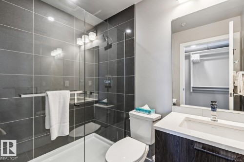 Bathroom featuring a glass-enclosed shower with dark gray tile surround, a white shower pan, and a three-light vanity fixture - 3302 10180 103 Street, Edmonton, AB - Indoor Photo Showing Bathroom