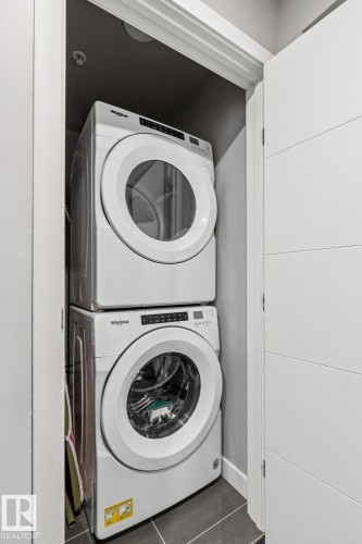 Integrated laundry closet featuring a stacked washer and dryer, finished with dark tile flooring - 3302 10180 103 Street, Edmonton, AB - Indoor Photo Showing Laundry Room